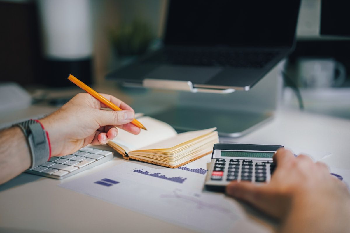 Contador trabalhando com calculadora, caderno e relatórios financeiros sobre a mesa